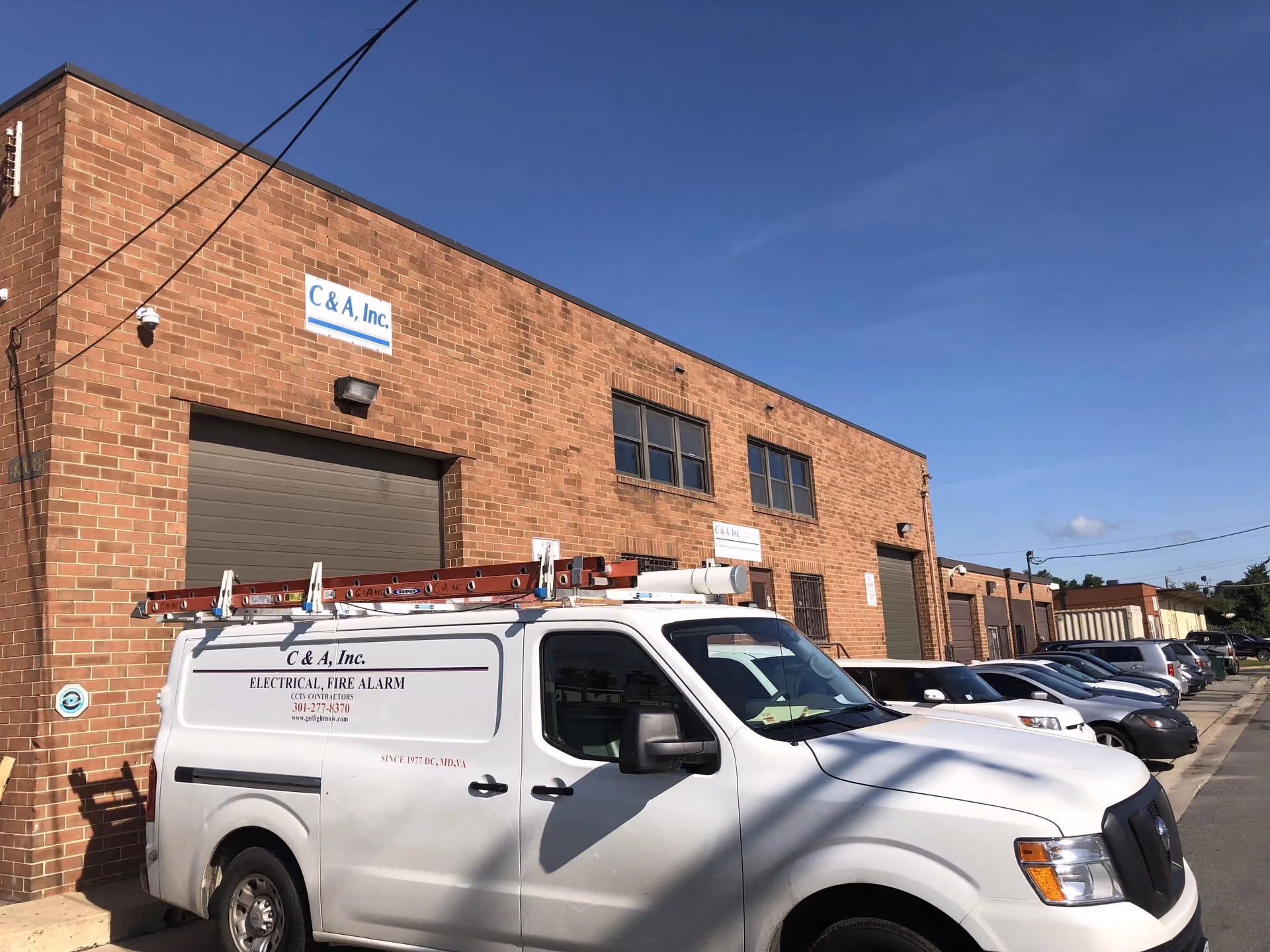 A C & A, Inc. service van with a roof ladder rack parked outside the company warehouse, the C & A sign mounted on the brick facade above the bay door.