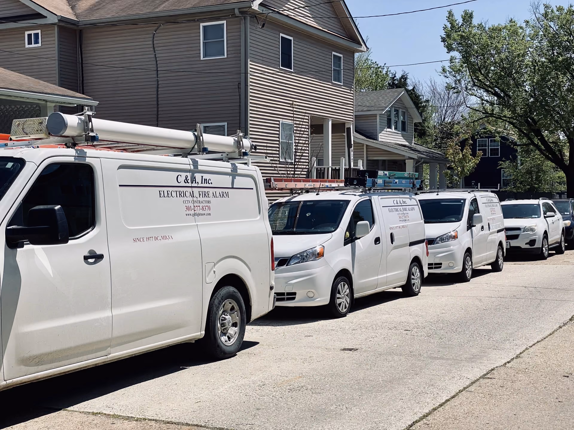 Three C & A service vans lined up along a residential street in front of a two-storey house.