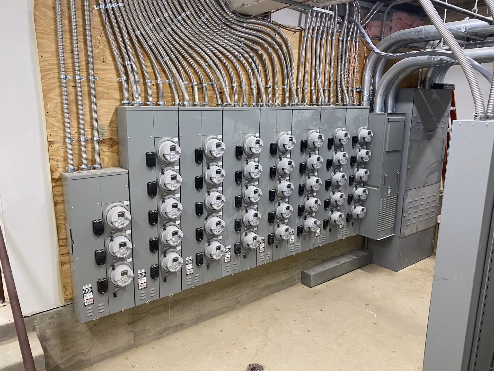 A multi-tenant utility meter stack with conduit risers running up the wall behind it.