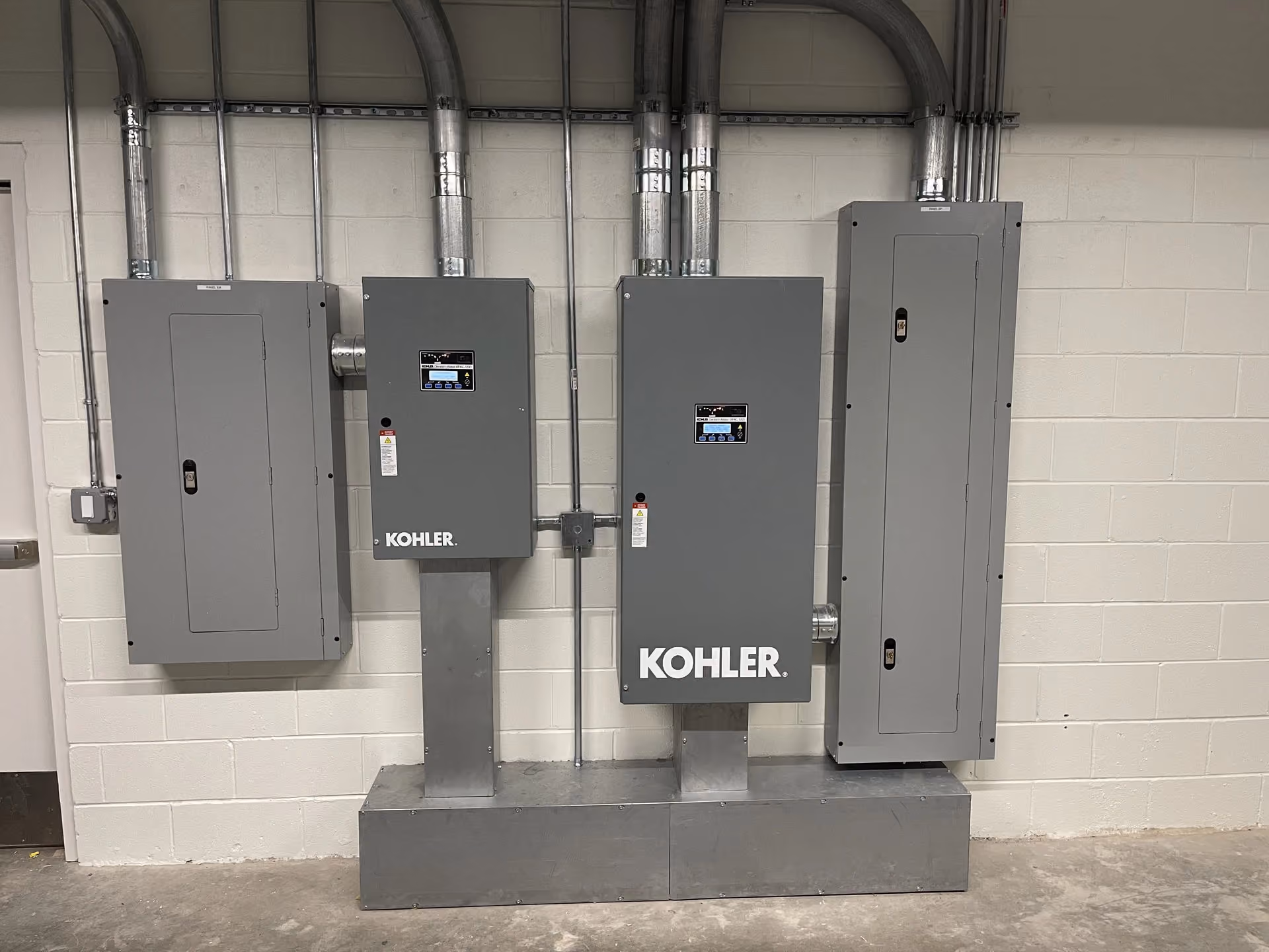 Two Kohler automatic transfer switches mounted on a shared concrete housekeeping pad between panelboards.